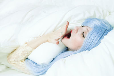 Smiling woman with dyed hair embracing pillow while lying on bed