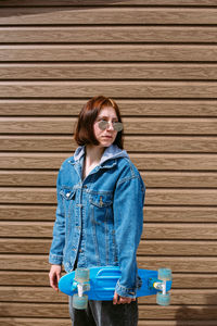 Young stylish woman wears sunglasses walks on the street with a skateboard