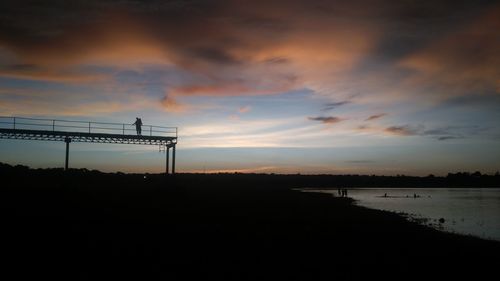 Silhouette bridge over lake against sky during sunset