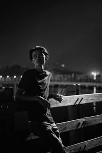 Portrait of young man sitting against illuminated sky at night