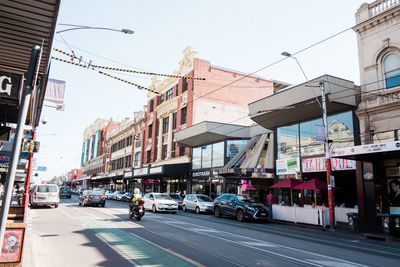 Cars on city street by buildings against sky