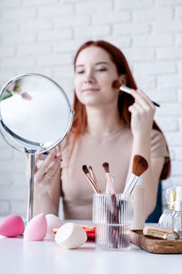 Young beautiful woman holding make-up brushes and making up with cosmetics set at home