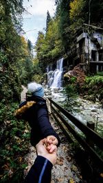 Man standing by waterfall in forest against sky