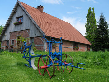 Bicycle by house on field against sky