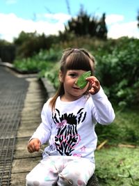 Portrait of girl holding leaf while sitting against plants