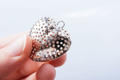 Close-up of hand holding heart shape decoration against white background