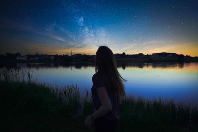 Woman standing by lake against sky at night