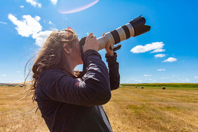 Woman holding umbrella on field against sky