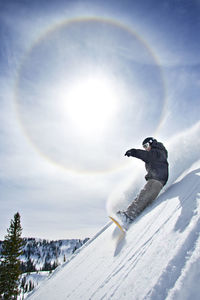 Man snowboarding on mountain against sky on sunny day