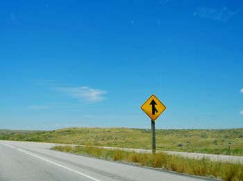 Empty road leading to country road against blue sky