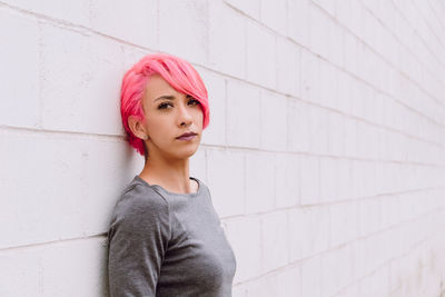 Pensive young female with dyed hair in casual clothes looking at camera while standing near white wall