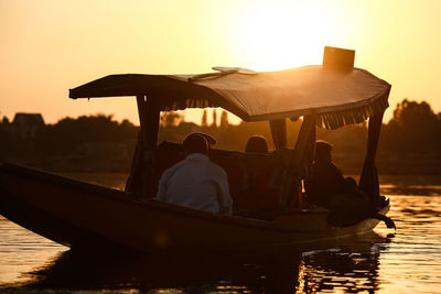 Man sitting on boat against sky during sunset
