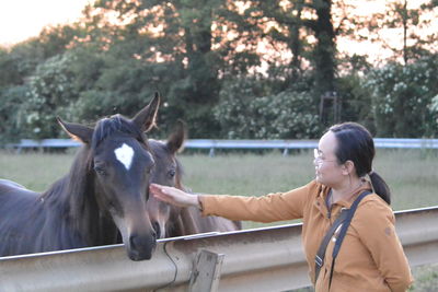 Smiling woman stroking horse at ranch