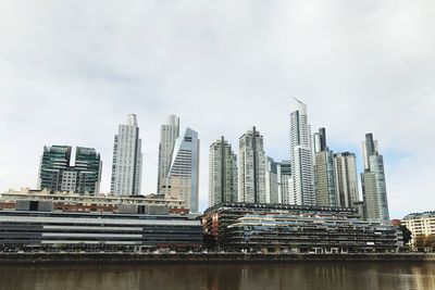 Modern buildings by river against sky in city