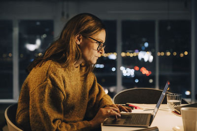 Ambitious businesswoman using laptop while working late at creative office