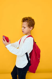 Side view of young woman standing against yellow background