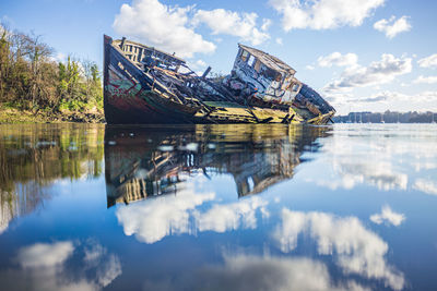 Reflection of abandoned boat in lake against sky