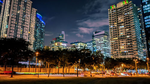 Illuminated buildings by street against sky at night