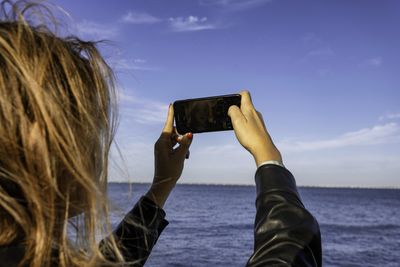 Rear view of woman photographing sea against sky