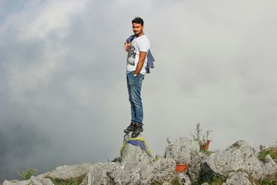 Woman standing on rock against cloudy sky