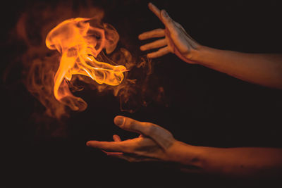 Cropped hands of person by flame against black background