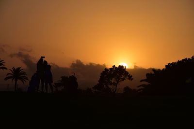 Silhouette man standing by palm trees against orange sky