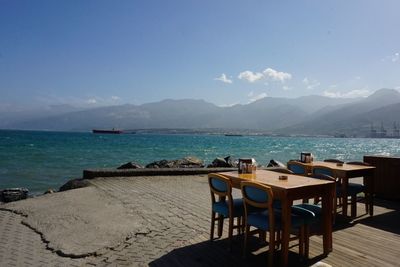 Empty chairs and table by sea against sky