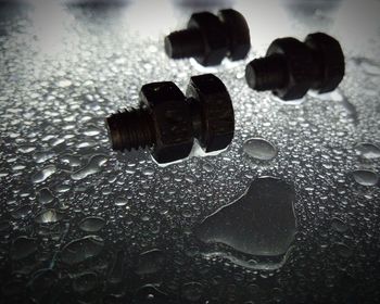 Bolts and nuts lie on a wet surface in drops of water in a creative photo