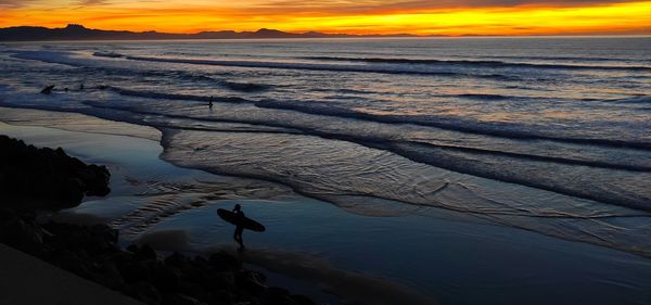 Scenic view of sea against sky during sunset with a surfer
