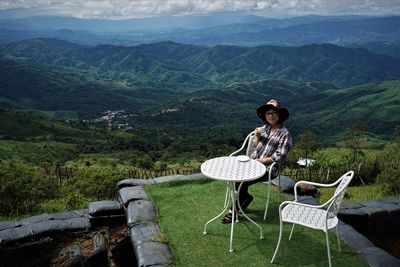 Portrait of senior woman having coffee while sitting on chair against mountains