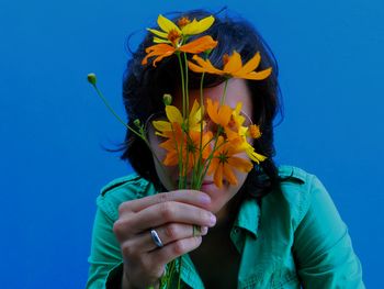 Close-up of woman holding yellow flower against blue sky