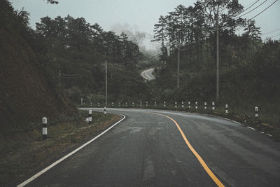 Empty road amidst trees against sky