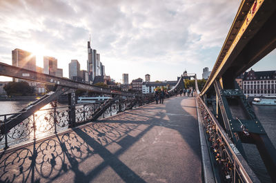 Bridge over river by buildings in city against sky