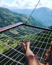 Low section of person relaxing on mountain against sky