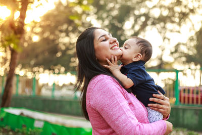 Side view of happy mother carrying son at park