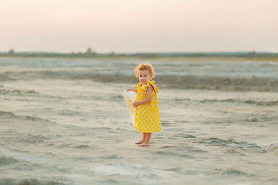 Girl standing on beach against sky during sunset