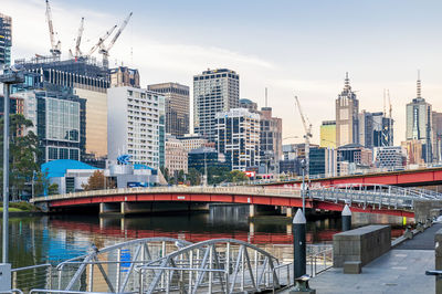 Bridge over river by buildings in city against sky