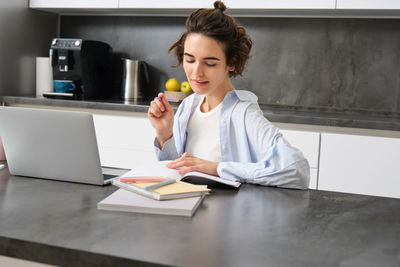 Young woman using mobile phone while sitting on table