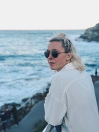 Portrait of woman wearing sunglasses while standing by sea against sky