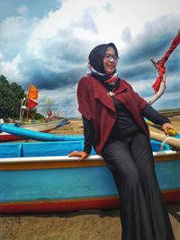 Woman looking away while sitting on boat at beach against sky