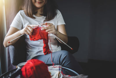 Midsection of woman knitting wool while sitting on chair