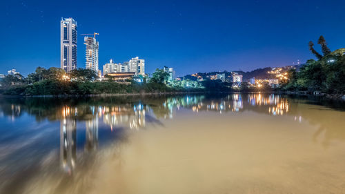 Scenic view of lake by illuminated buildings against sky at night