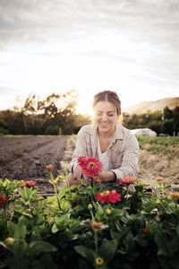 Happy female farmer working on flowering field against sky