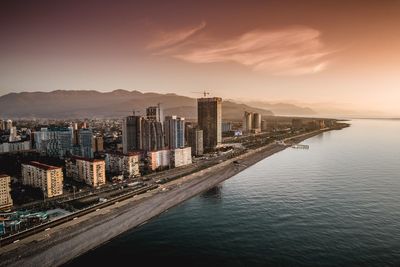 Modern buildings by sea against sky during sunset