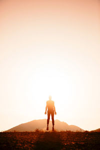 Silhouette man jumping on field against clear sky during sunset