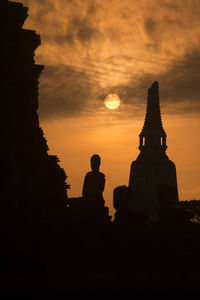 Low angle view of silhouette temple and buddha statue against sky during sunset