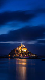 Illuminated mont saint michel with reflection in sea against sky