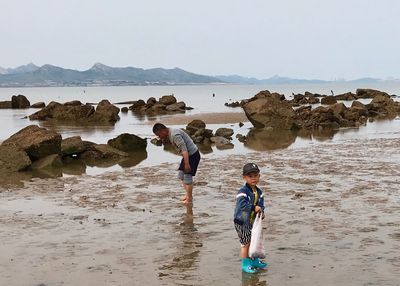 People on rocks at beach against sky