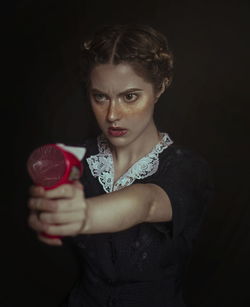 Angry young woman holding equipment against black background