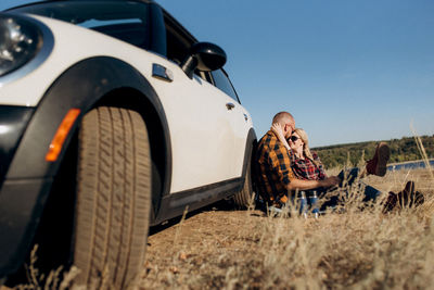 Full length of man sitting on car against sky